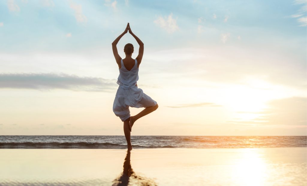 A guest practising yoga by the water at sunrise